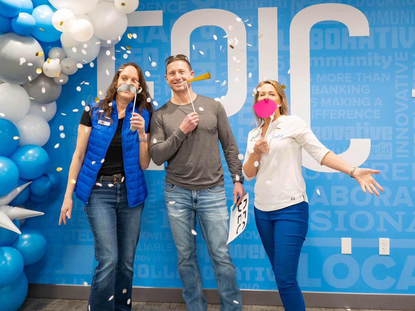 Three people smiling and posing in front of a wall that says Epic during the D. E. C. ribbon cutting event.