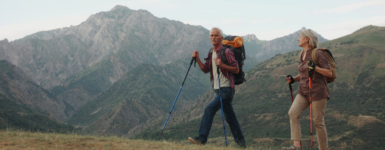 Older man and woman backpacking and hiking up a mountainside.