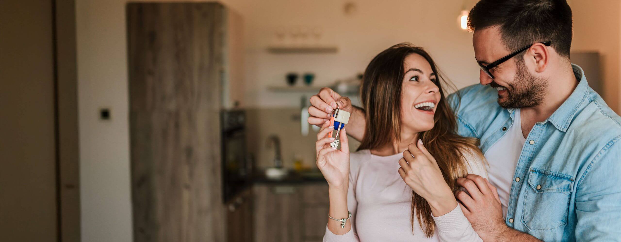 Man smiling with one arm around a woman and the other arm handing her a house key.