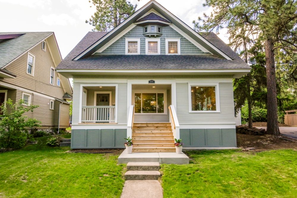 Exterior of an older, cottage style home with a pavement path leading up to a wooden stairs onto a porch.