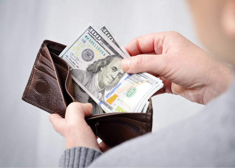 Man holding a brown leather wallet and placing two hundred dollar bills inside.