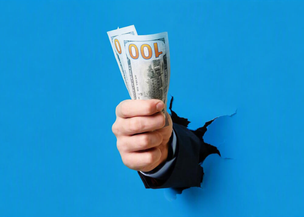 Hand breaking through a blue wall toward the viewer, holding two one hundred dollar bills.